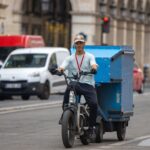 Cargo-bike courier riding through traffic with a large blue delivery box