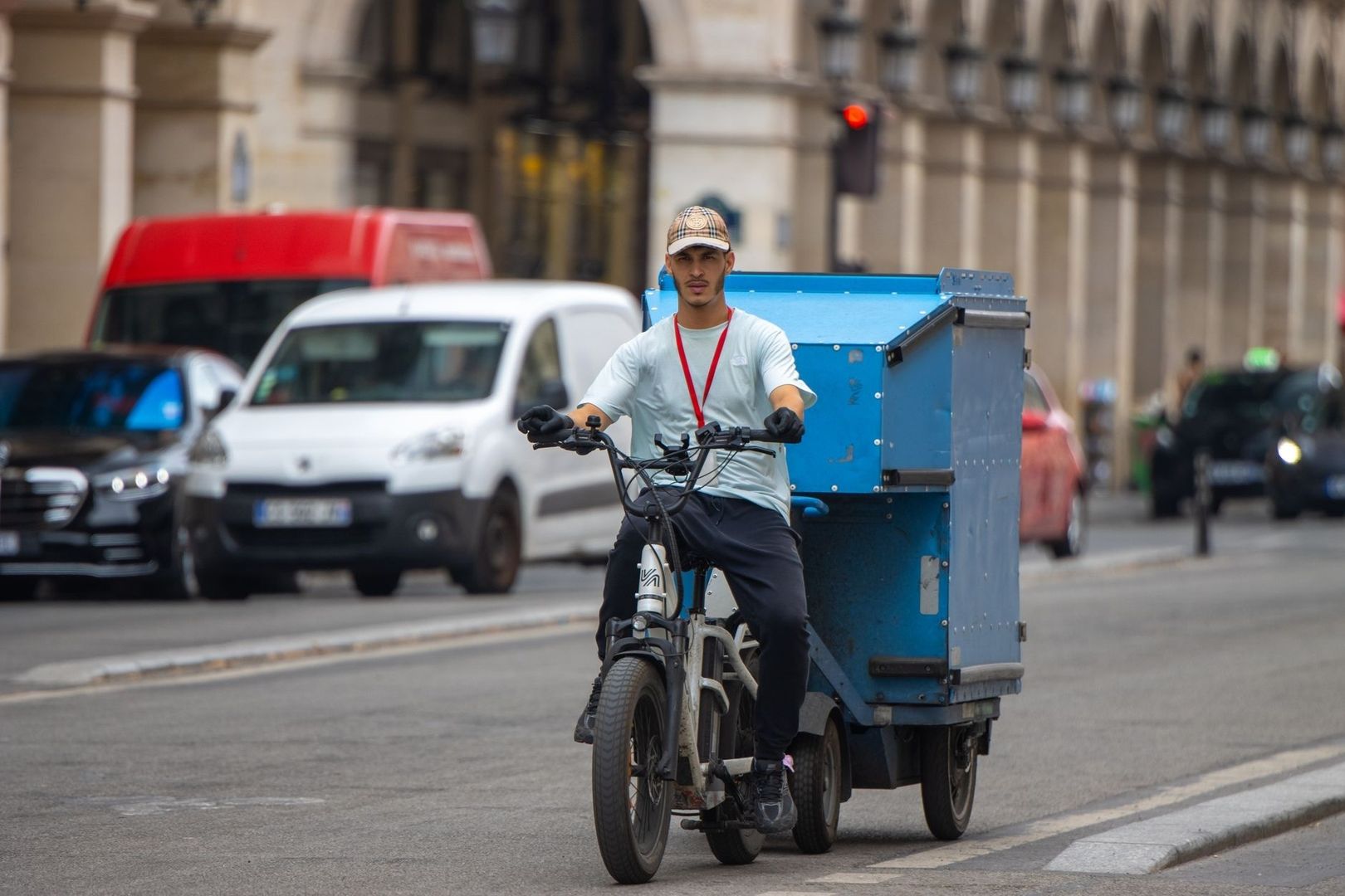 Cargo-bike courier riding through traffic with a large blue delivery box